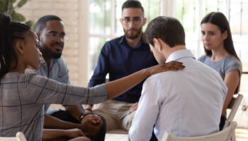 A support group comforting an individual during a talk therapy session, one of the treatments for drug-induced psychosis