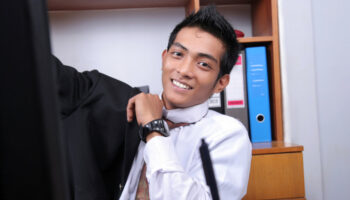 A smiling office worker puts on a jacket while sitting at their desk