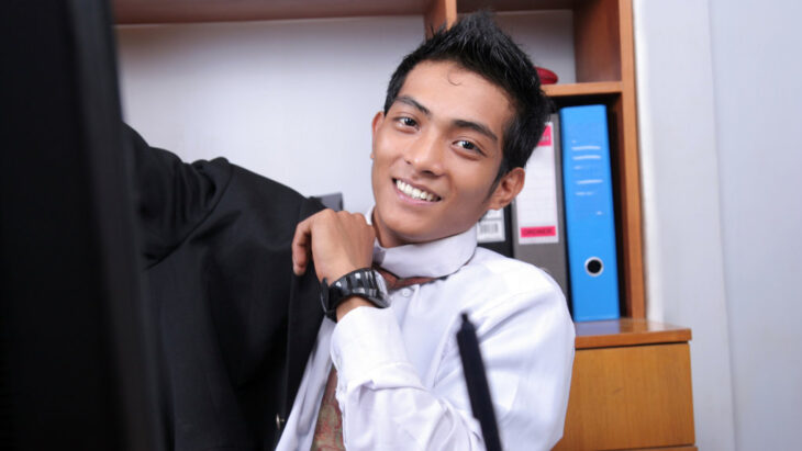 A smiling office worker puts on a jacket while sitting at their desk