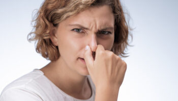 A woman grips her nose, possibly facing sinus issues as a side effect of cocaine addiction