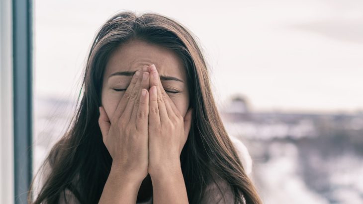 An anxious woman grips her face in a stressful fashion