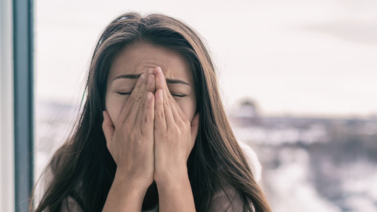 An anxious woman grips her face in a stressful fashion