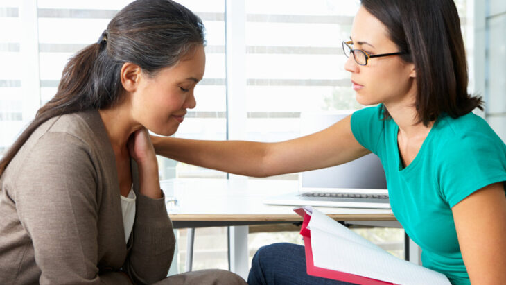 A woman consoles another person by placing a hand on her shoulder