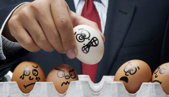 A man in a suit places an egg with an anxious face drawn onto it into a carton