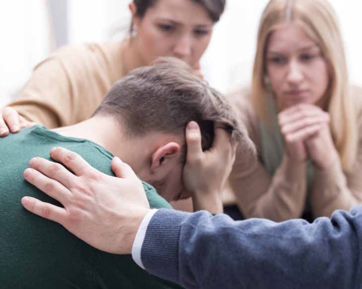 A stressed out man being comforted by someone else during a meeting