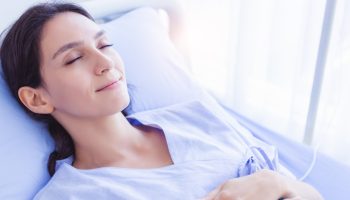 A peaceful looking woman smiles and relaxes in a hospital bed, recovering.