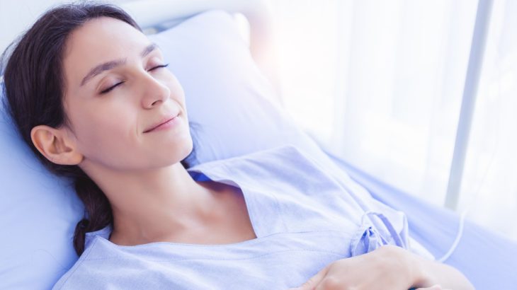 A peaceful looking woman smiles and relaxes in a hospital bed, recovering.