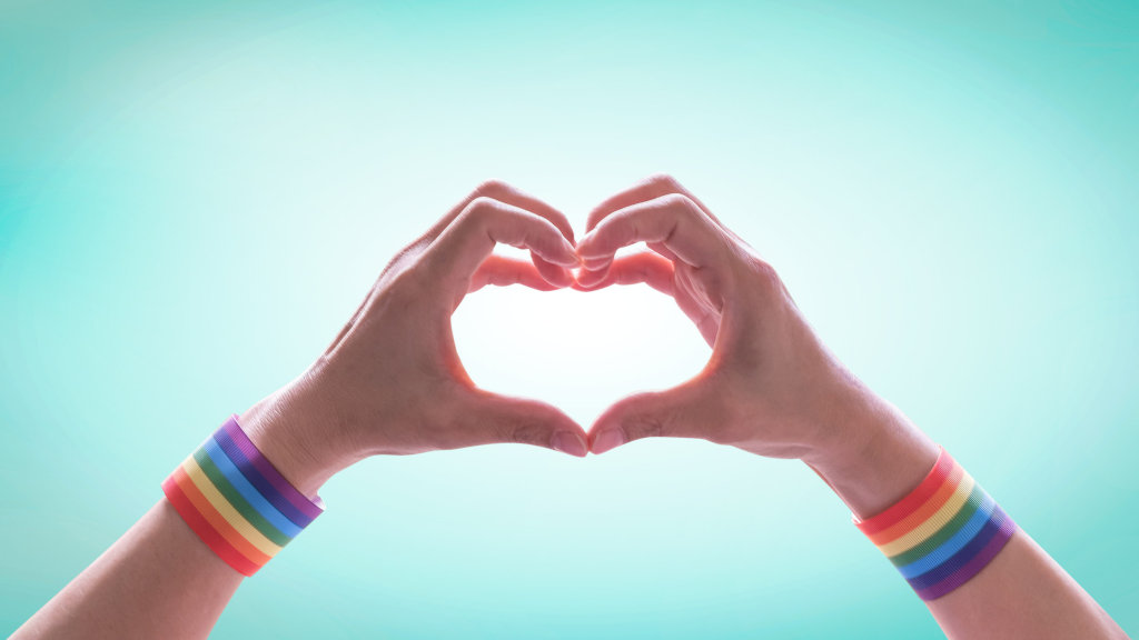 A pair of hands with rainbow pride flags on the wrist, suggesting LGBTQ+ pride