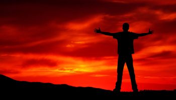 A person stands defiantly with their arms raised, promoting a sense of hope and accomplishment