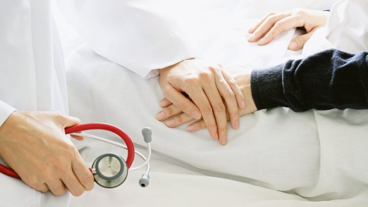 A doctor lays a hand on a patient's hand