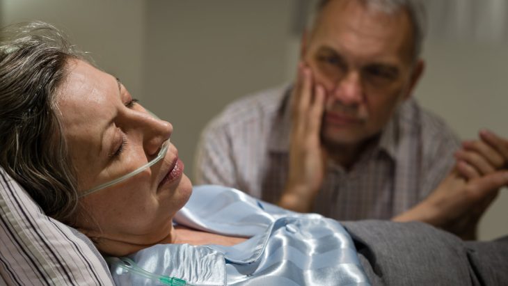 A man holds the hand of a woman who is in a coma