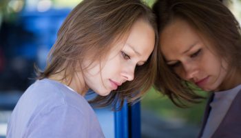 A woman leans against a mirror, looking depressed at her own reflection