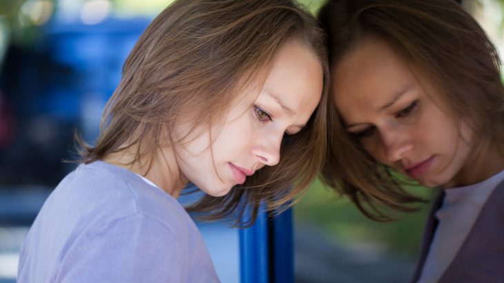 A woman leans against a mirror, looking depressed at her own reflection