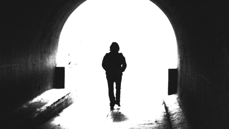 A person with their back turned walks away, exiting a tunnel and stepping into the light