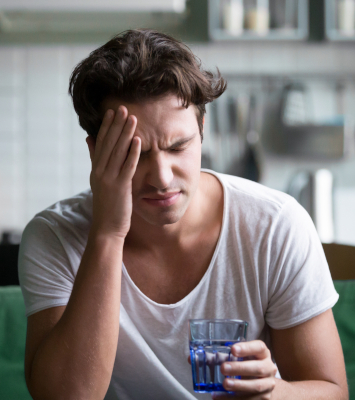 A young adult man clutches his head in pain