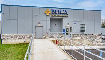 Boca Recovery in Huntington, Main entrance in a modern building with logo above front door. Ramp leading up to door with green grass to the right and blue skies above.