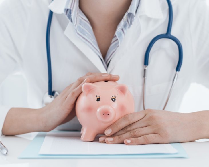 A doctor sitting with a piggy bank in their hands