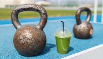 A green detox smoothie with dumbbells on a running track