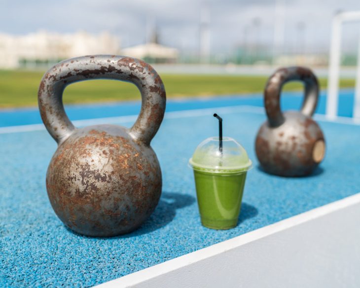 A green detox smoothie with dumbbells on a running track