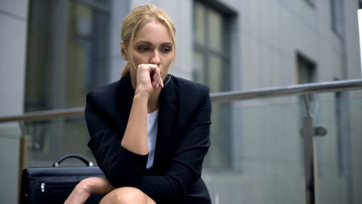 A businesswoman looks down at the ground, with an anxious or depressed expression