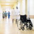 A view inside a hospital, with and empty wheelchair and care providers in the background