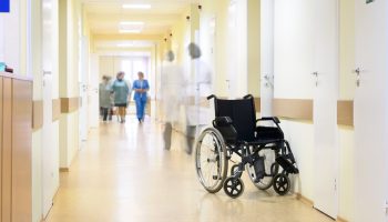 A view inside a hospital, with and empty wheelchair and care providers in the background