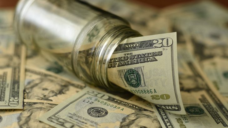 A jar full of money, sitting atop a pile of twenty dollar bills