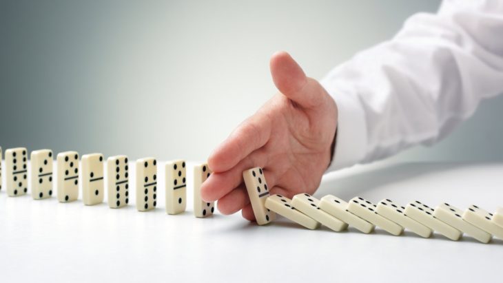 A person inserts their hand to prevent a line of dominos from falling