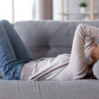 A woman lying on a couch clutches her forehead