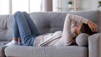 A woman lying on a couch clutches her forehead
