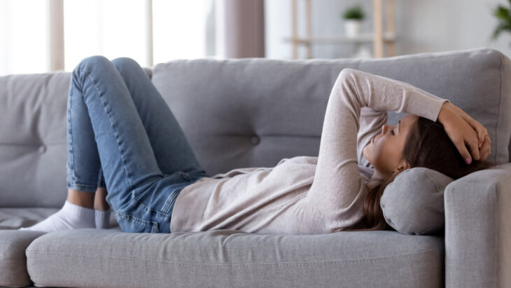 A woman lying on a couch clutches her forehead