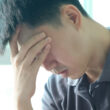 A stressed out looking man grips his forehead, possibly suffering from withdrawal symptoms during detox