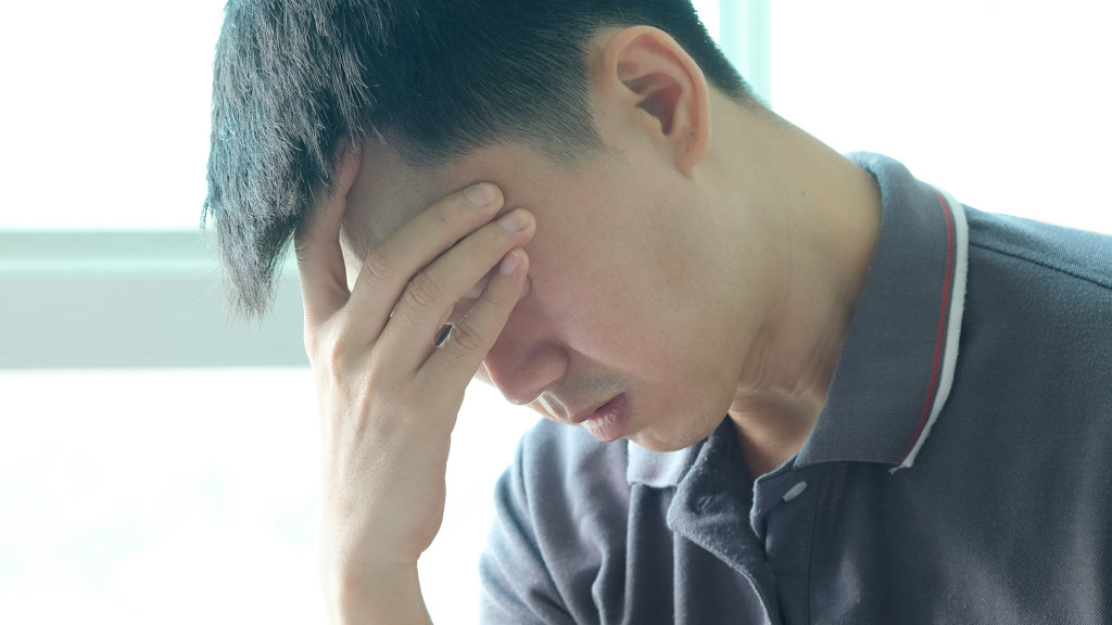 A stressed out looking man grips his forehead, possibly suffering from withdrawal symptoms during detox