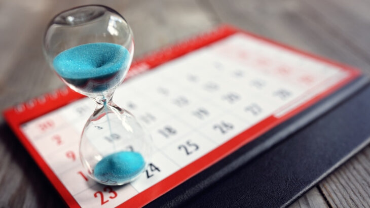 A calendar with an hourglass sitting atop it