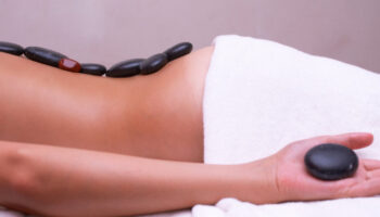 A person lying on a bed, with hot stones on their back as part of a holistic treatment regimen