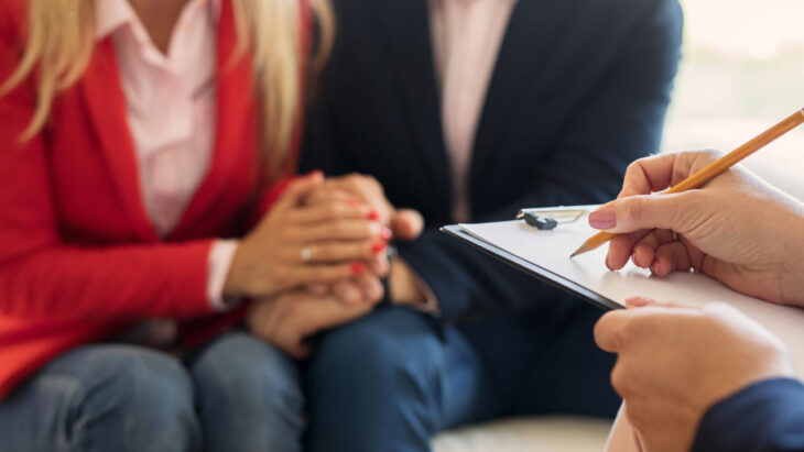 A doctor writes on a clipboard while speaking with a couple. Learn more about couples rehab here.