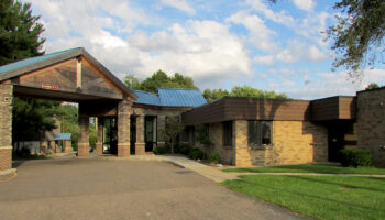Exterior view of treatment facility main entrance with brick construction, metal roof, covered entrance area, and landscaped grounds