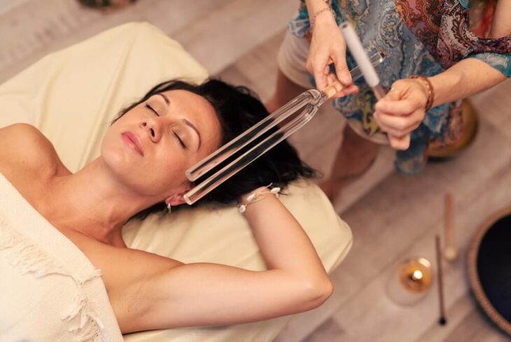 A woman lying on a massage table near a tuning fork. Learn more about holistic practices in traditional detox programs here.