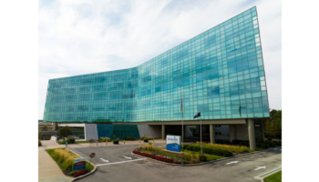 Exterior of contemporary medical facility with curved glass facade, landscaped grounds, and parking area