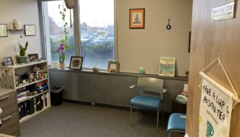 Interior counseling office with large windows overlooking parking area, seating chairs, plants, and inspirational wall decor