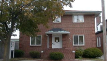 Exterior view of brick residential building with white entrance door, multiple windows, and landscaping