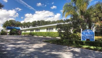 Exterior view of single-story treatment facility with white building, palm trees, landscaping, and facility signage