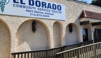 Exterior view of El Dorado Community Service Center showing cream-colored stucco building with arched entryway, wooden ramp, and facility signage displaying address and phone number