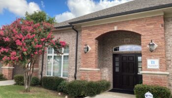 Exterior view of brick treatment facility with arched entry, black doors, flowering pink tree, and landscaped grounds