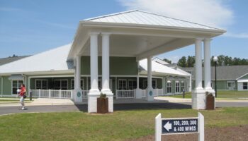 Exterior front entrance with covered portico, white columns, and green siding visible