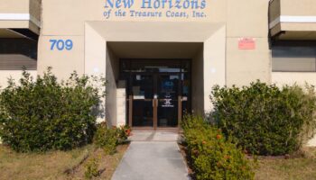 Exterior front entrance of New Horizons treatment facility showing blue signage, address number 709, landscaping, and concrete walkway