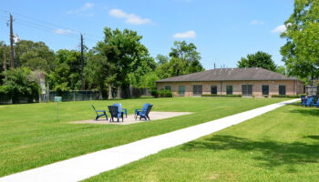 Exterior view of facility grounds with manicured lawn, concrete pathway, Adirondack chairs, and brick building with multiple windows
