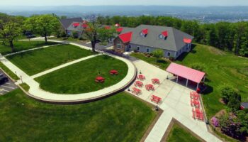 Exterior aerial view of treatment facility showing main buildings with red metal roofs, landscaped grounds, circular gathering areas, and surrounding grounds