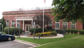 Exterior view of red brick institutional building with white entrance portico, columned entry, and landscaping
