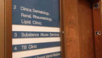 Interior hallway directory sign for Building 90 listing lobby and clinical departments including substance abuse services and TB clinic